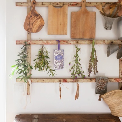 Tábuas de cortar de madeira e ervas secas penduradas num ladeiro rústico de madeira com utensílios de cozinha