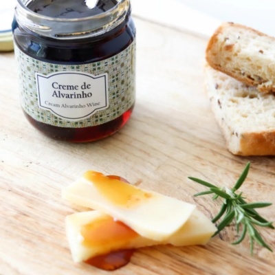 Frasco de creme Alvarinho com fatias de queijo, pão e ramo de alecrim sobre tábua de madeira