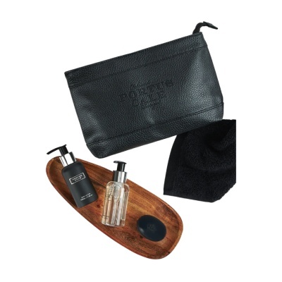 Conjunto de produtos de higiene pessoal com bolsa de couro preta, frascos com dispensador, sabonete, toalha preta e bandeja de madeira