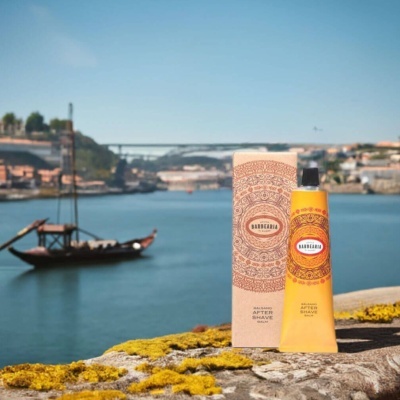 Bálsamo after shave em tubo amarelo com embalagem decorativa e rio com barco ao fundo