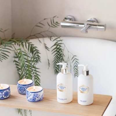 Produtos de banho Portus Cale em frascos brancos com dispensador e velas azuis acesas junto a uma banheira branca
