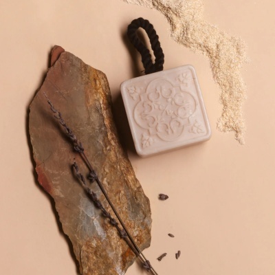 sabonete quadrado branco com relevo decorativo e corda preta junto a pedra castanha e lavanda seca