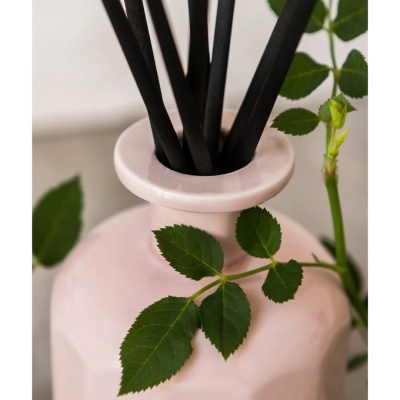 Frasco difusor cerâmico rosa com varetas pretas e folhas verdes