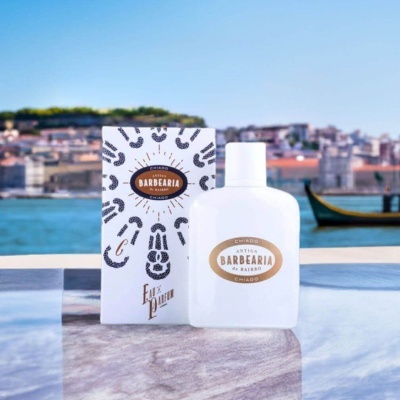 Frasco branco fosco de perfume com embalagem branca e padrões pretos, em fundo de paisagem de rio e cidade