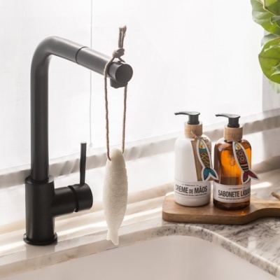 Torneira preta com esponja pendurada e duas embalagens de creme e sabonete sobre base de madeira