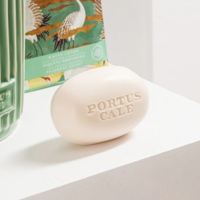 Sabonete oval creme PORTUS CALE sobre superfície branca com embalagem verde ao fundo