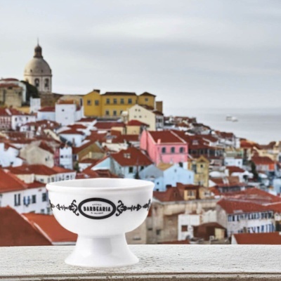 Taça branca de cerâmica com decoração preta e texto ANTIGA BARBEARIA DE BAIRRO com vista urbana ao fundo