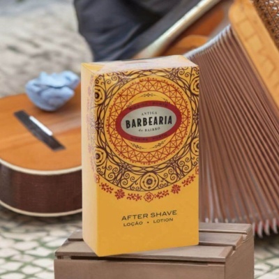Embalagem amarela de after shave Antiga Barbearia de Bairro pousada sobre caixa castanha com guitarra ao fundo