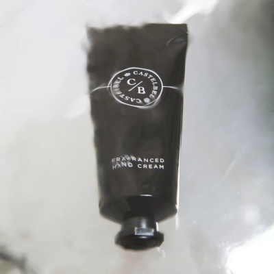 Tubo preto fosco de creme de mãos aromatizado com texto CASTELBEL C/B sobre superfície cinzenta.