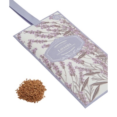 Saco perfumado de tecido com padrão floral lilás e etiqueta central com texto, e pilha de fragmentos marrons ao lado.