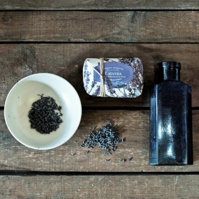 Sabonete aromático de lavanda, flores secas escuras em prato branco e garrafa preta sobre mesa de madeira