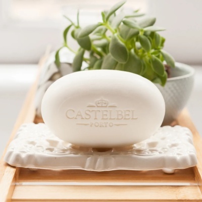 Sabonete oval branco com texto CASTELBEL PORTO em suporte cerâmico branco decorado e planta em vaso cinzento