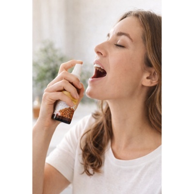 Mulher aplica spray oral num frasco com etiqueta amarela e imagem de própolis