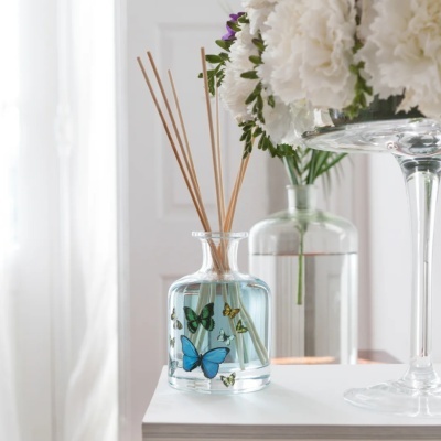 Difusor de aromas em vidro com borboletas coloridas e flores brancas ao lado