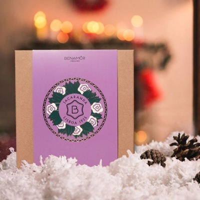 Embalagem de papel castanho com etiqueta roxa e design floral, em ambiente com neve e pinhas.