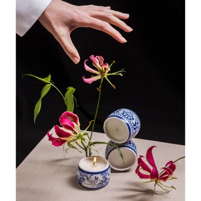 Velas cerâmicas azuis decorativas com flores rosas e mão sobre mesa bege.