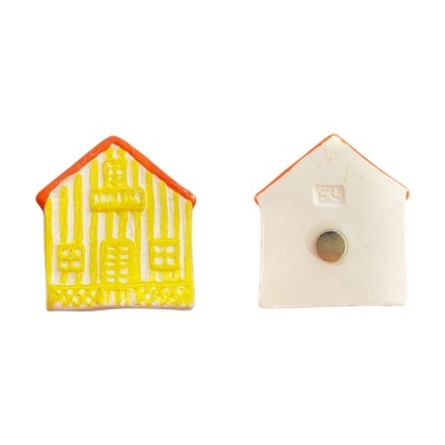 Imã de geladeira em forma de casa amarelo com telhado laranja e verso branco com peça metálica.