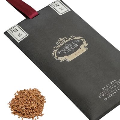 Saqueta perfumada preta com fita vermelha e texto decorativo, junto a bagas secas castanhas