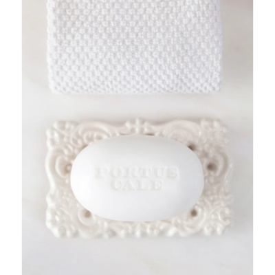 Sabonete branco PORTUS CALE numa saboneteira creme decorada com toalha branca ao fundo