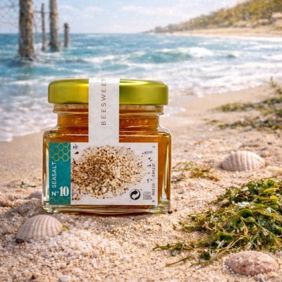 Frasco de vidro com tampa dourada sobre areia e conchas na praia