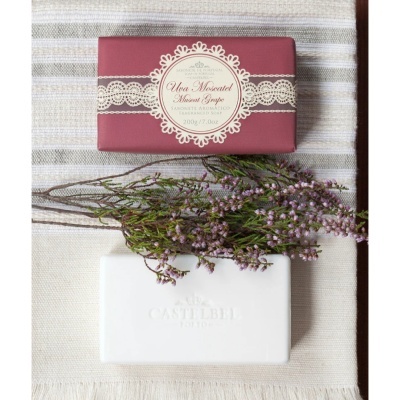 Sabonete Castelbelle com embalagem vinho, ramo de flores lilases e sabonete branco gravado