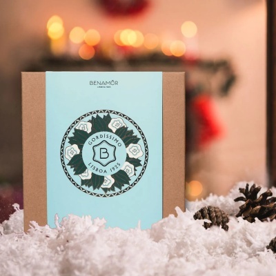 Caixa de papel com rótulo azul claro e decoração floral, neve artificial e pinhas à frente