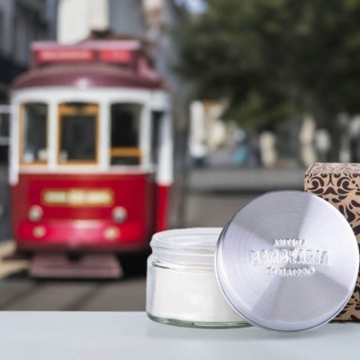 Pote de creme em vidro com tampa metálica ao lado de uma caixa decorada e elétrico vermelho desfocado ao fundo