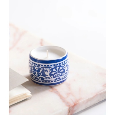Vela branca em recipiente cerâmico azul com padrão branco sobre mármore branco