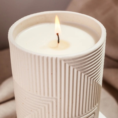 Vela branca acesa em recipiente cerâmico branco texturizado