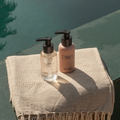 Dois frascos de produtos PORTUS CALE sobre toalha bege junto a piscina