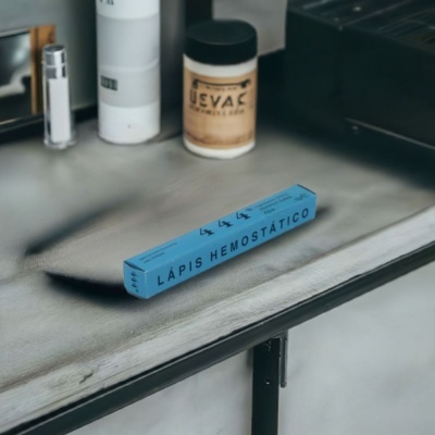 Caixa azul de lápis hemostático numa bancada metálica com frascos desfocados ao fundo.