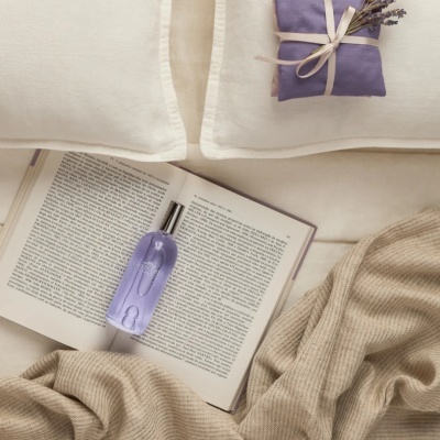 Garrafas de perfume castelbel lavanda sobre livro aberto com almofadas e manta