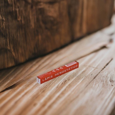 Estojo vermelho com lápis hemostático sobre madeira clara