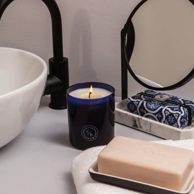 Vela perfumada azul, sabonete bege e embalagem azul e branca num lavabo minimalista