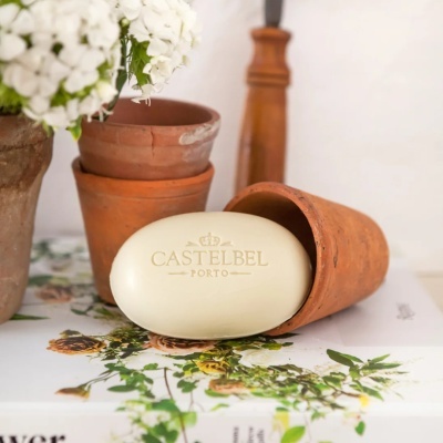 Sabonete oval creme CASTELBEL PORTO sobre livro floral com vasos de barro e flores brancas