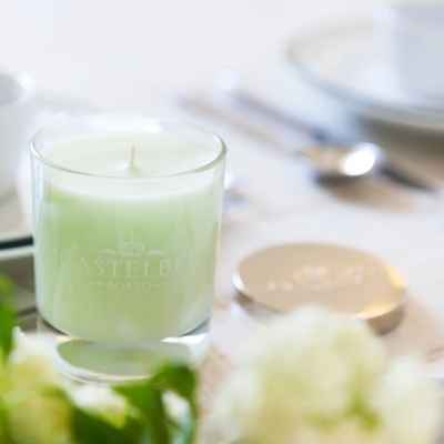 Vela aromática verde claro em copo de vidro com inscrição CASTELBEL PORTO e tampa metálica ao lado.