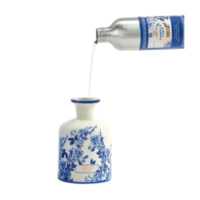 Frasco cerâmico branco com padrão azul e líquido a ser vertido de garrafa metálica