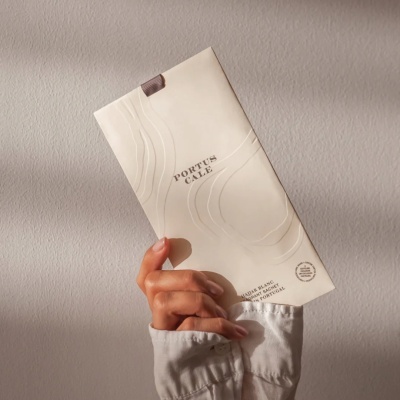 Saco de fragrância bege claro com relevo e texto PORTUS CALE nas mãos.