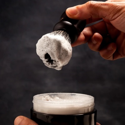 Pincel de barbear com espuma branca sobre frasco preto aberto