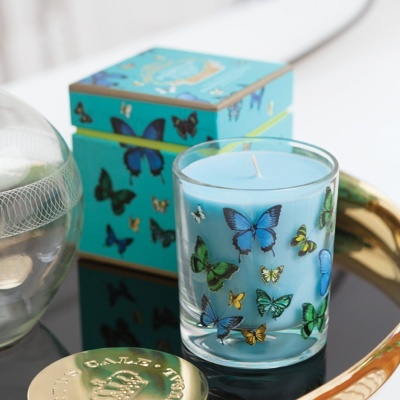 Vela azul clara em copo de vidro decorado com borboletas coloridas com caixa azul ao fundo