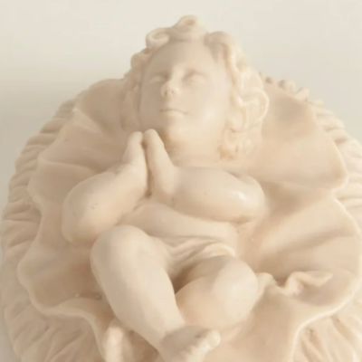 Estatueta de bebé claro em pose de oração sobre base ondulada