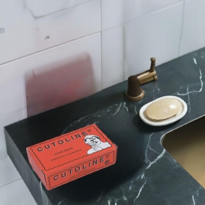 Saboneteira branca com sabonete e caixa vermelha Cutoline numa bancada de mármore preta com torneira bronze