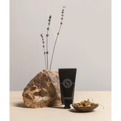 Tubo preto de creme para mãos ao lado de rocha, prato com flores secas e caules secos no fundo