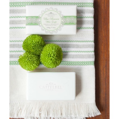 Sabonete aromático branco embalado com faixa verde, flores verdes e sabonete branco sobre tecido listrado branco com verde e cinza e fundo de madeira