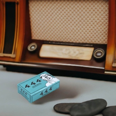 Caixa azul de creme pós-barba com ilustração e texto, rádio vintage de madeira ao fundo