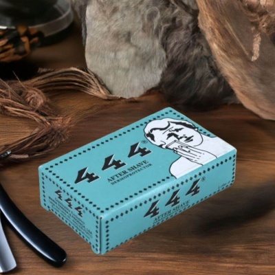 Caixa azul de after shave 444 com rosto masculino e texto preto sobre mesa de madeira com objetos em pele e navalha