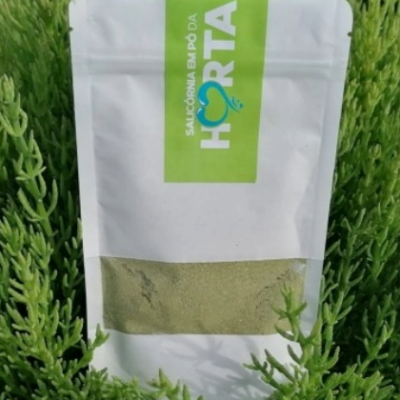 Embalagem branca de pó verde com rótulo verde em meio a folhas verdes.