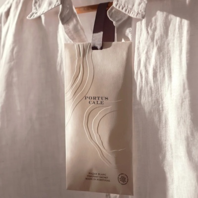 Sachet perfumado branco PORTUS CALE pendurado em cabide com roupa branca.