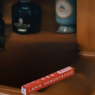 Caixa vermelha de lápis hemostático em superfície de madeira com frascos ao fundo