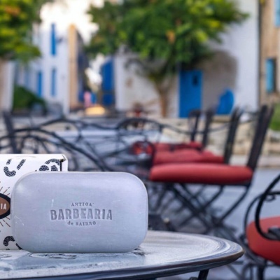 Sabonete ANTIGA BARBEARIA de BAIRRO numa mesa metálica ao ar livre com cadeiras pretas e almofadas vermelhas